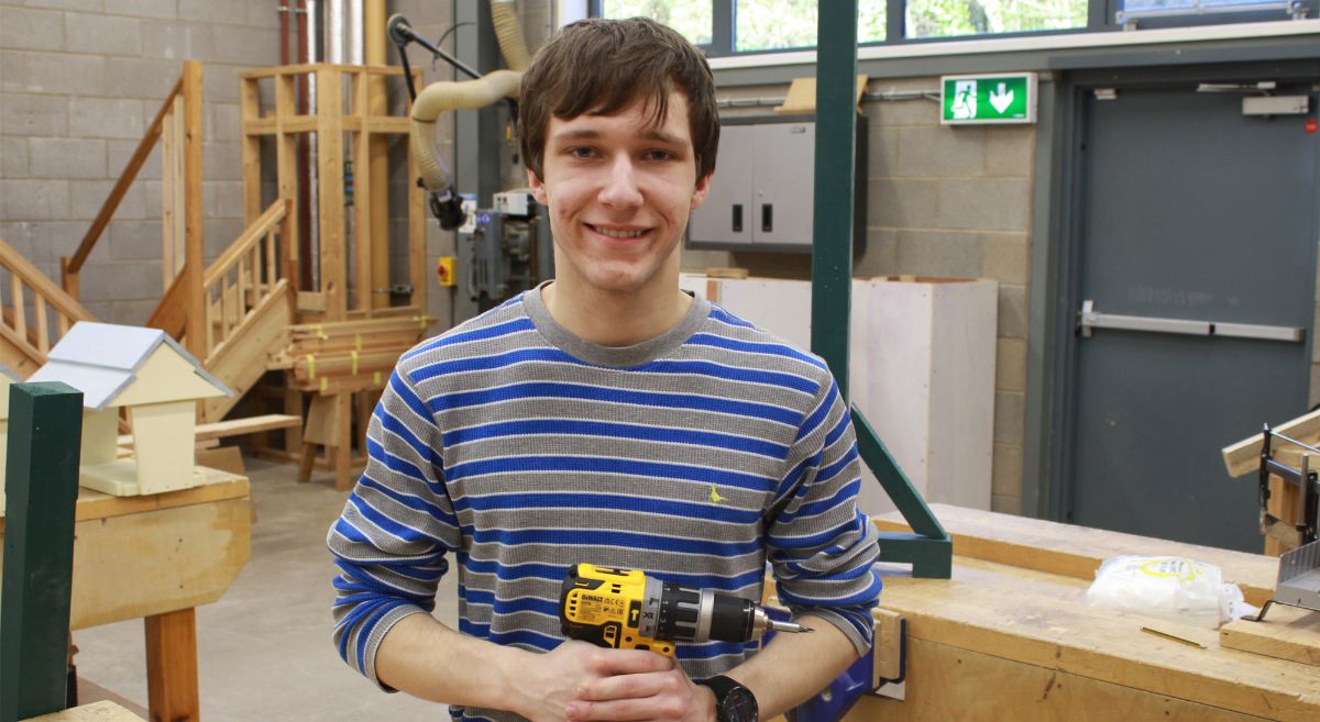 Matthew Wales, young man with dark hair wearing strippy top holding drill in workshop